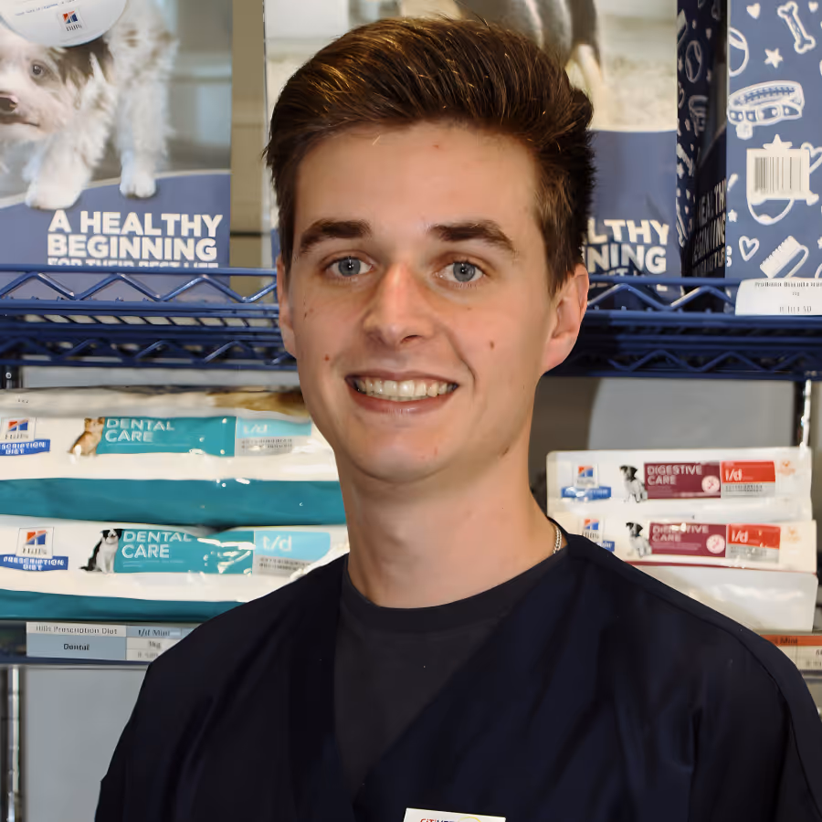 Young veterinarian smiling at Citivet with pet food bags on shelves behind him.